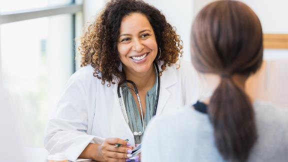 A smiling mid adult female doctor listens as a female patient discusses her health.