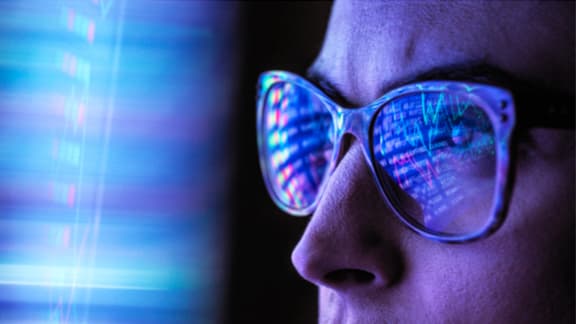 Close-up of a person looking at code, with the code reflected on her glasses.