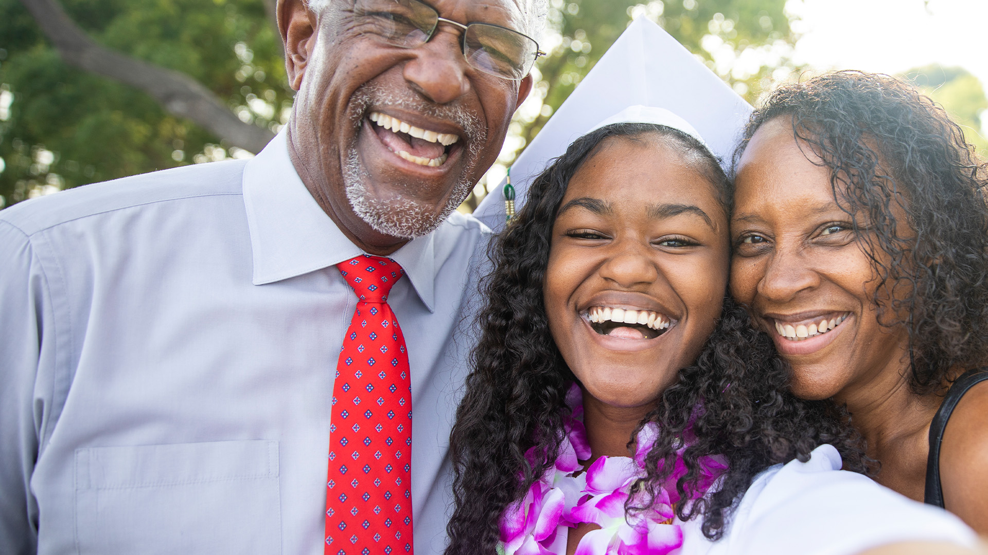 A young college graduate smiling for a selfie with her parents on graduation day.