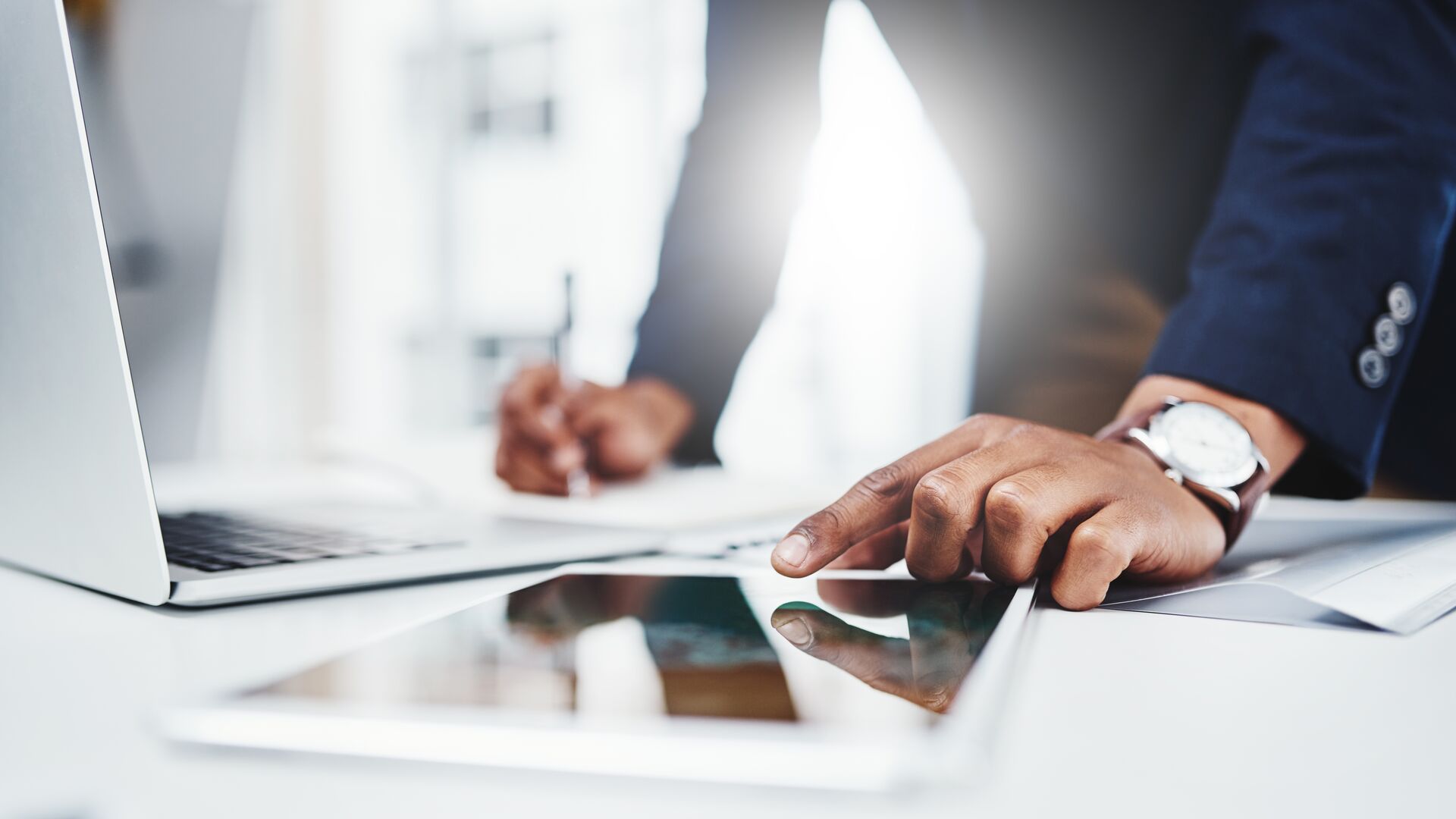 A man writing and looking at a laptop.