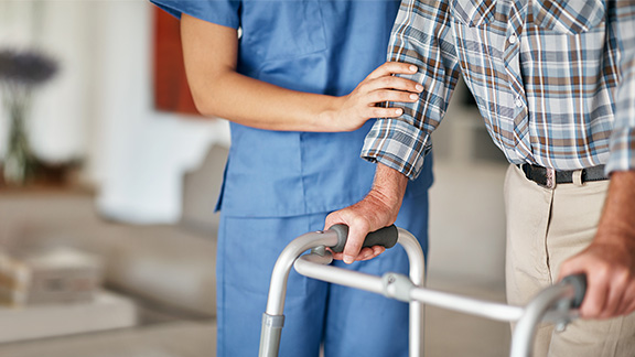 A nurse assisting an elderly person who is using a walker for support