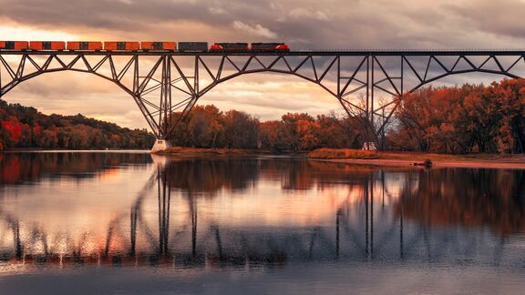 Autumn train moving across a bridge with reflections.