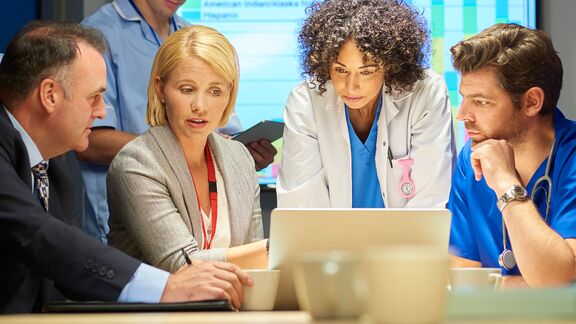 A mixed group of healthcare professional and business people meet around a conference table.