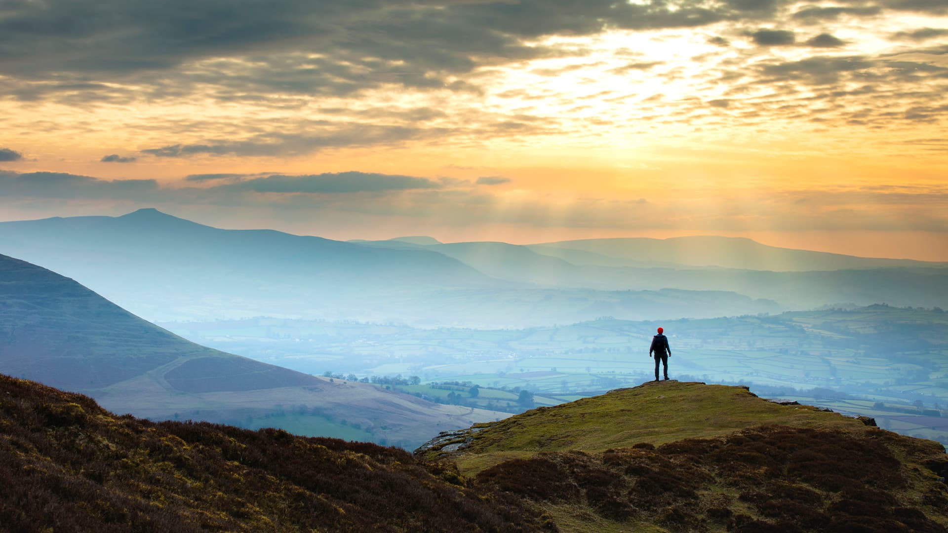 A person in the distance standing on a mountain and looking at the sunset.