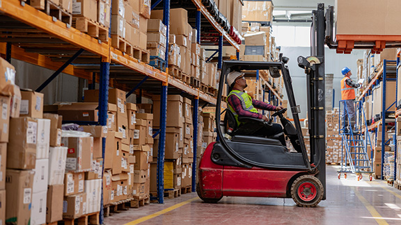 A worker using heavy machinery to move large pallets around.