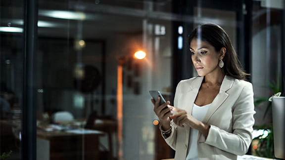 A woman looking at her phone with a city skyline in the background at night.