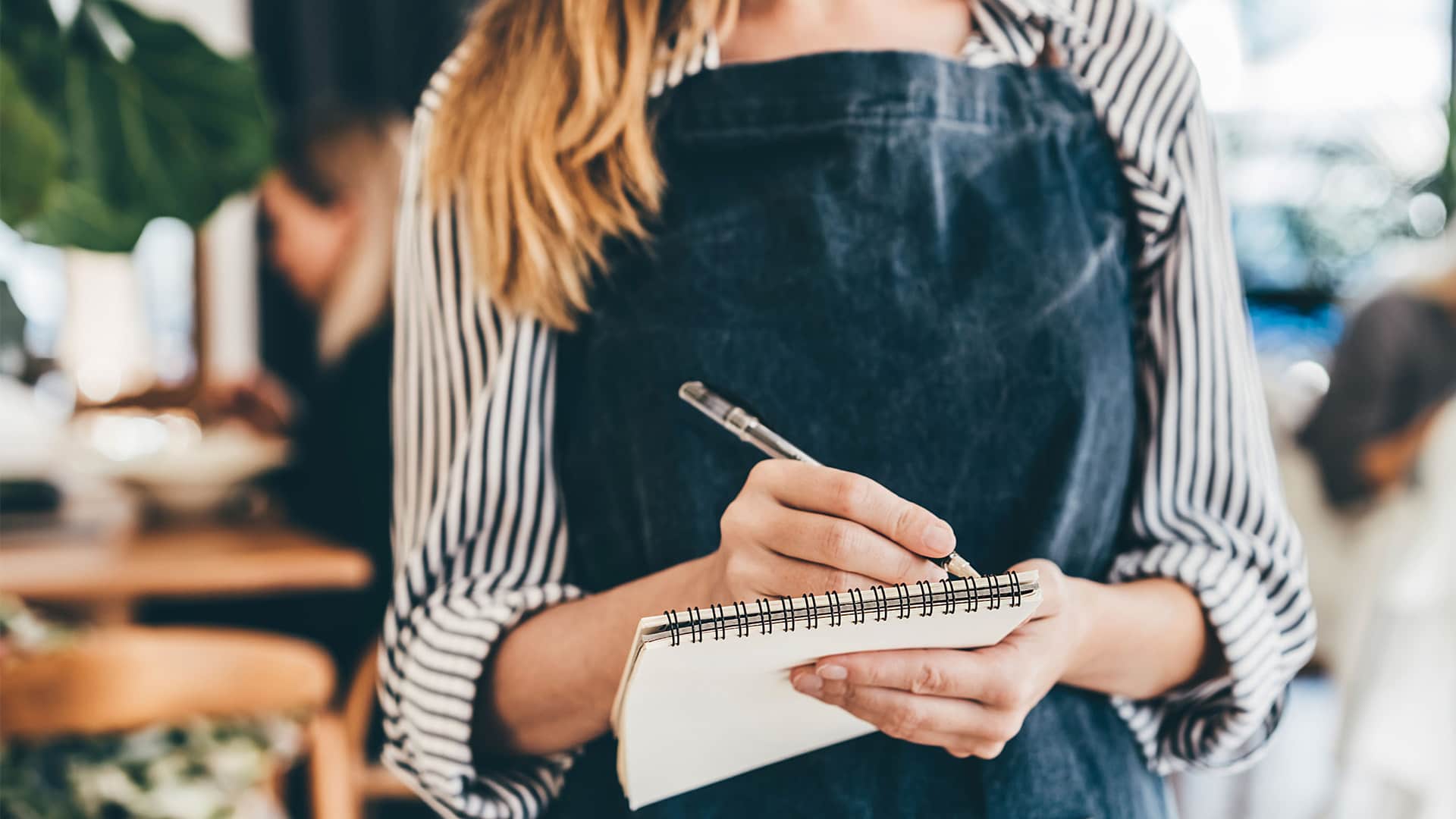 A woman working as a server at a restaurant, taking down a customers order.