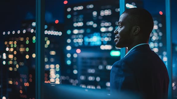 Man in a suit standing by a large window at night, looking out over a city skyline, representing financial oversight and credit risk governance in banking.