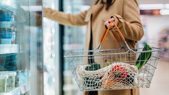 A woman looking in the dairy aisle at a grocery store while carrying a basket.