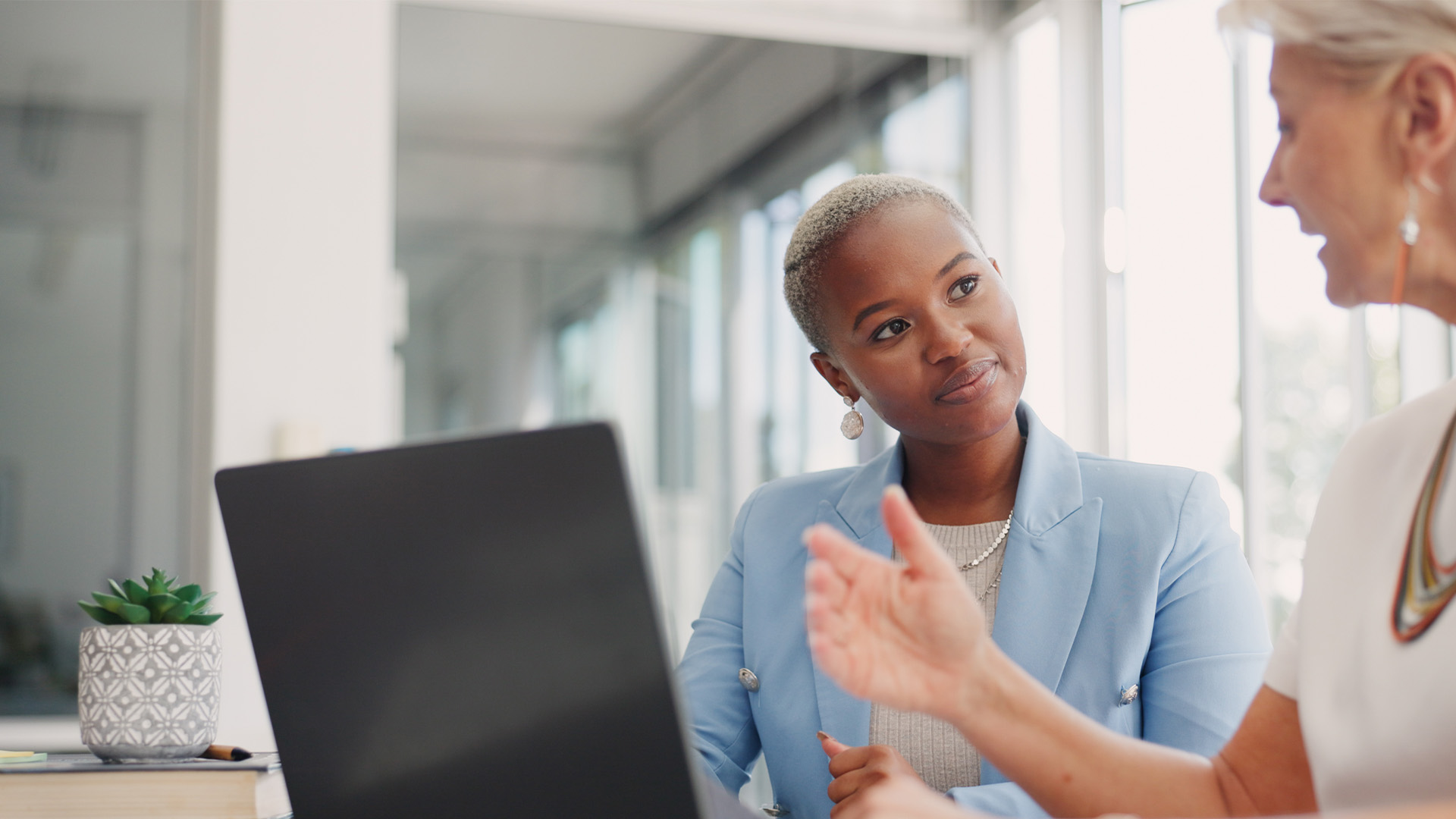 Two female work colleagues chatting in front of a laptop.