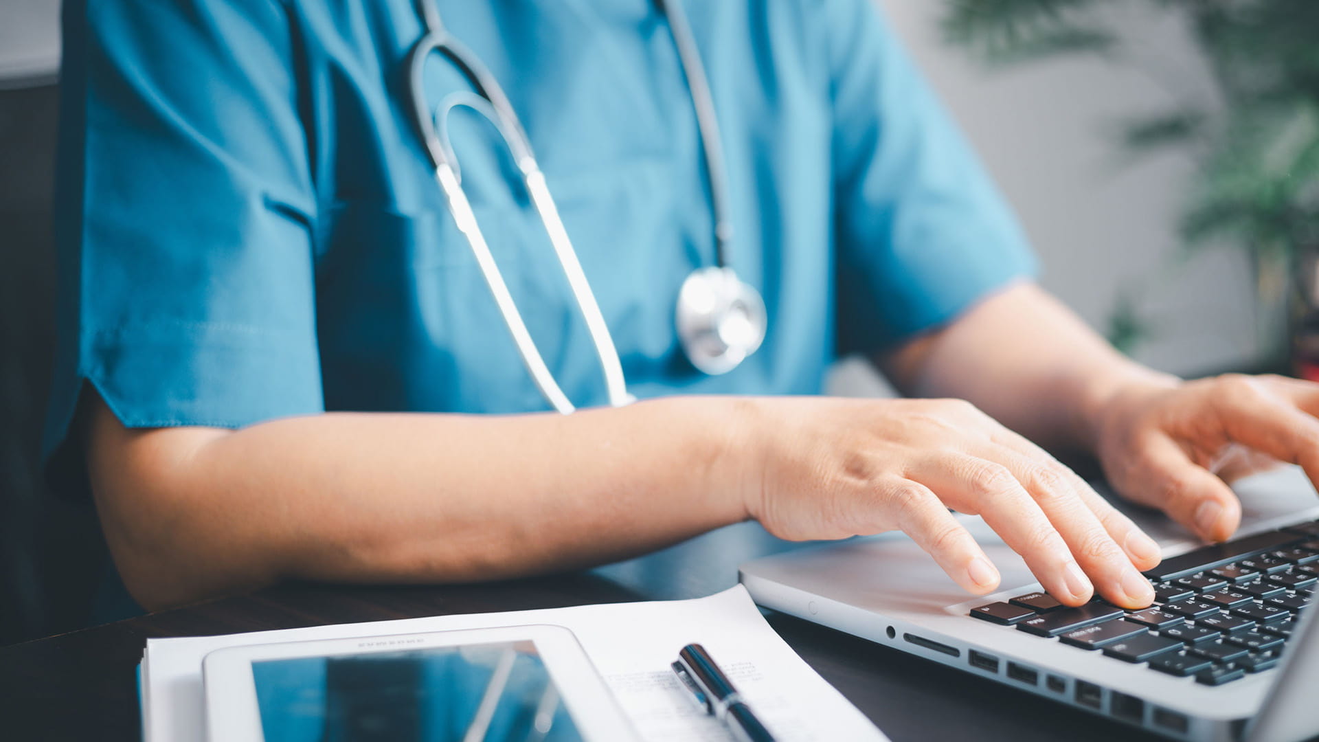 A healthcare worker typing at a laptop.
