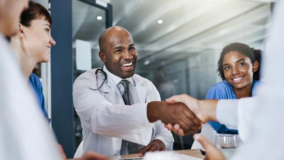 Doctors and nurses smiling and shaking hands after a successful surgery.