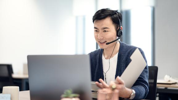 A man wearing a headset on a conference call on his work laptop.