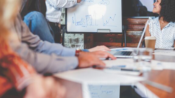 A person using a white board to give a presentation to a group of people in an office.
