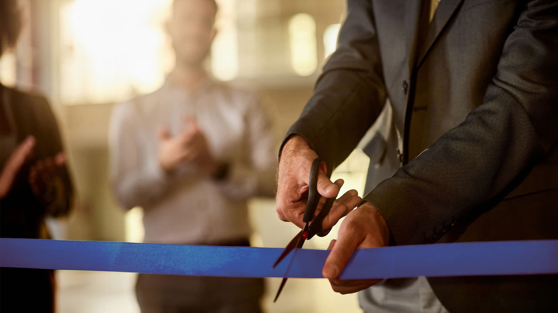 Close up of unrecognizable male CEO cutting ribbon during opening ceremony of the new company.