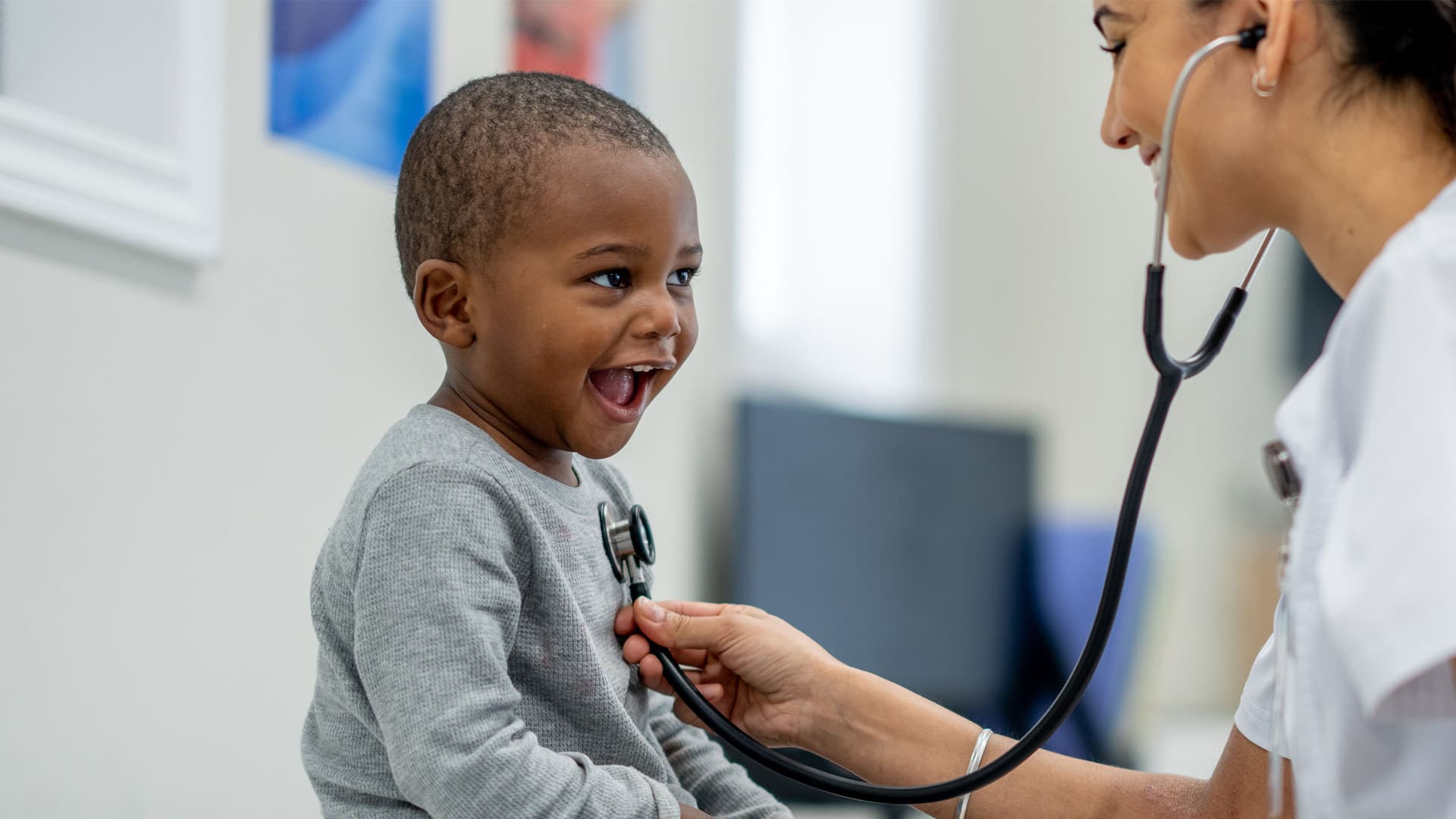 A little boy smiling at his doctor while she checks his heartbeat with a stethoscope.