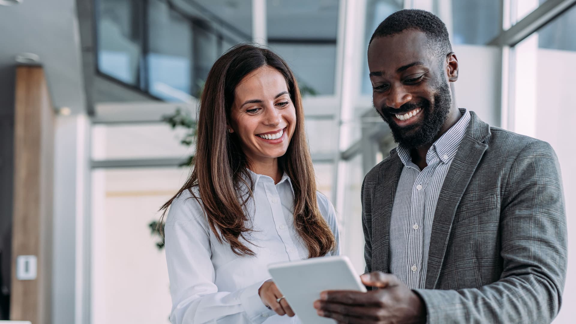 Two people who are smiling and looking down at a digital tablet together