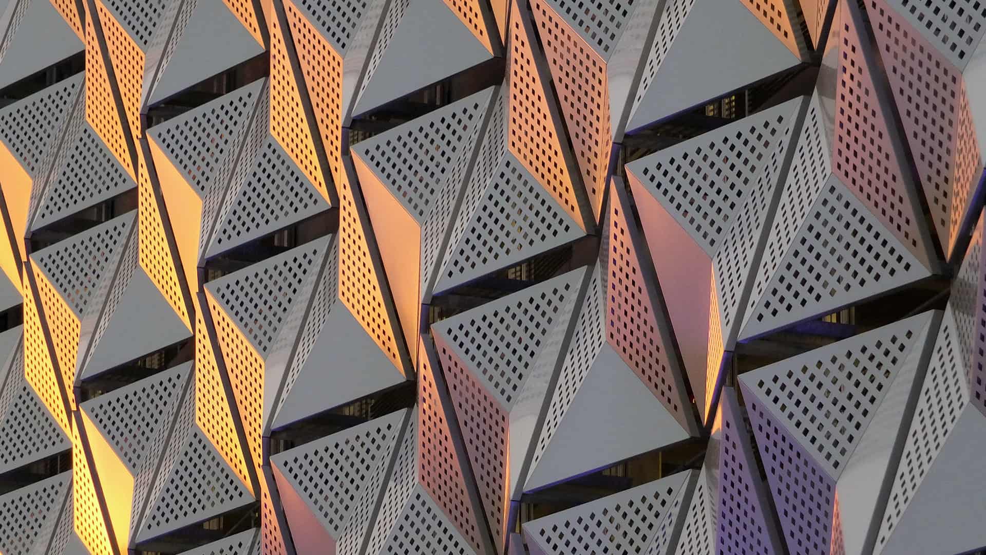 Modern steel cladding with angular geometric patterns and square holes in a shiny metallic finish with colored reflection on the wall of a car park in leeds