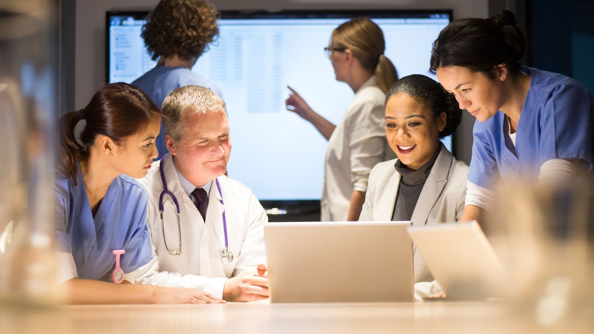 Four medical professionals review data on a laptop.