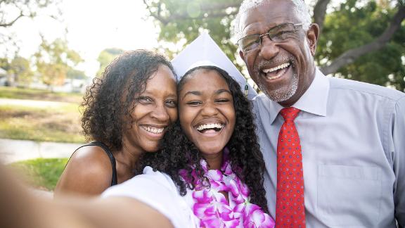 A young college graduate smiling for a selfie with her parents on graduation day.