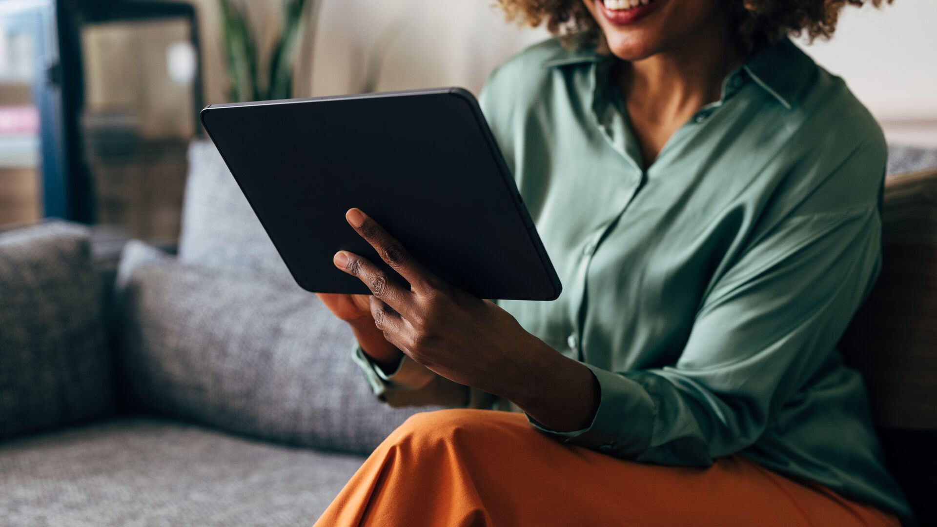 A woman sitting on her couch and looking at a tablet.