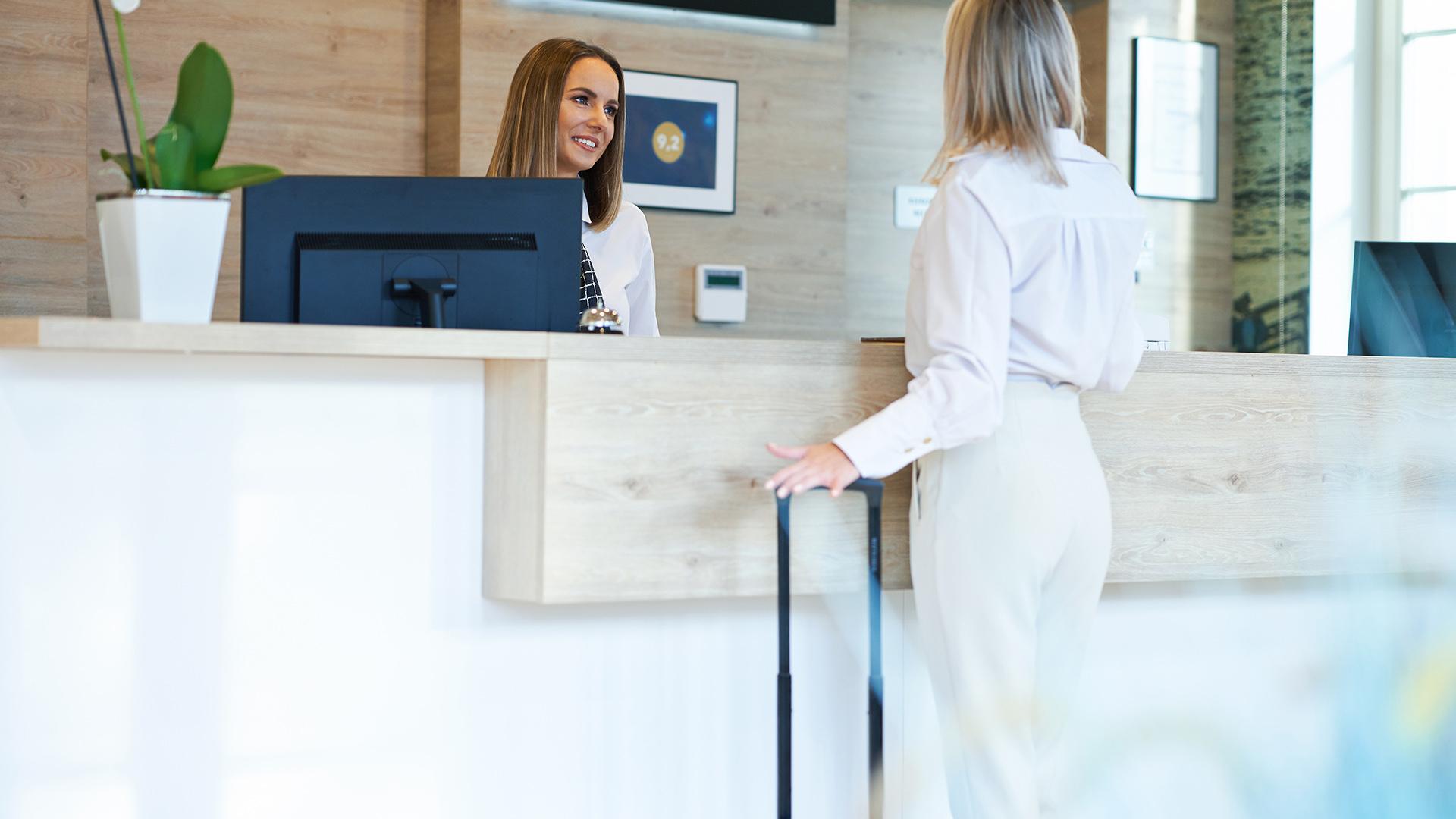 Receptionist and businesswoman at hotel front desk.
