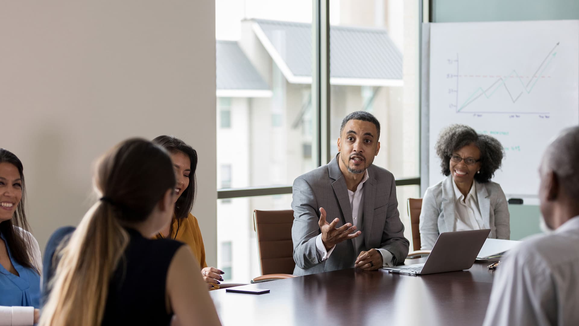 Mid adult businessman gestures as he discusses sales with a group of colleagues during a meeting.