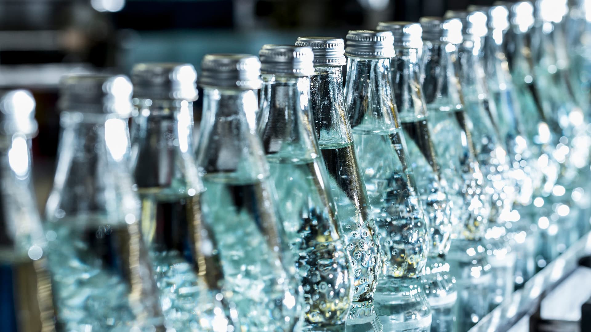 Glass bottles on an assembly line being filled with sparkling water.