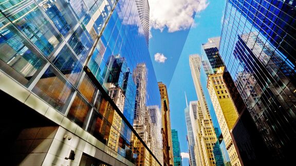 Low‑angle view of tall glass skyscrapers reflecting neighboring buildings and a blue sky with scattered clouds.