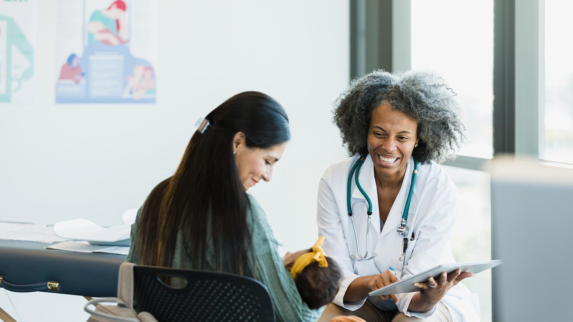 In the middle of a discussion about test results, the mature adult doctor and the new mom smile when the baby girl makes a noise.