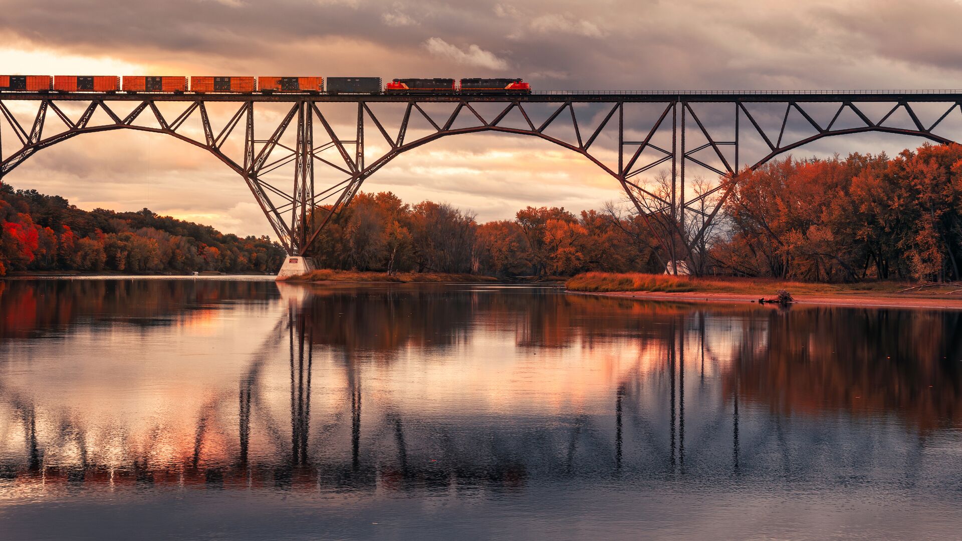 Autumn train moving across a bridge with reflections.