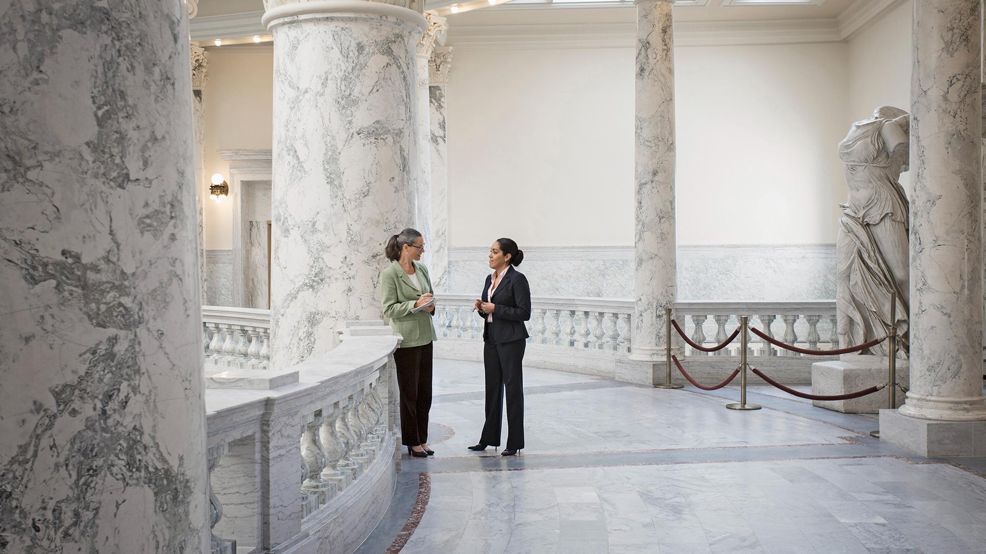 Two female politicians who are talking in a government building